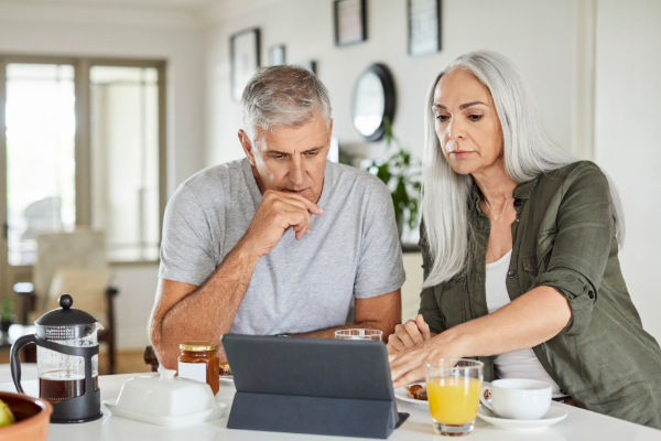 a couple in their 60s looking at a laptop sitting at the kitchen counter