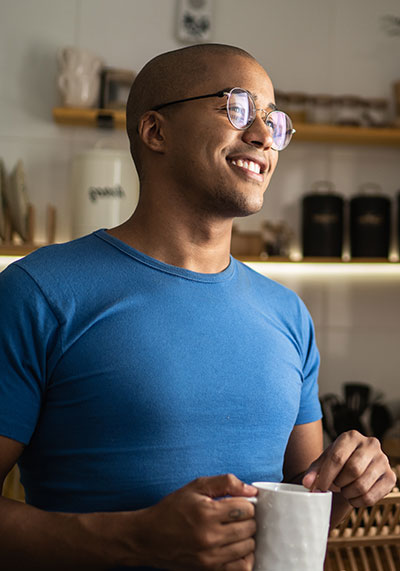 a male in his 30s wearing a blue shirt smiling and holding a coffee cup