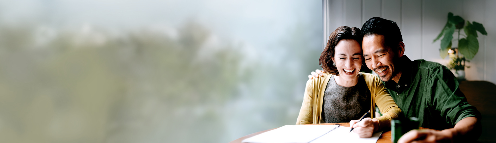 husband and wife laughing and sitting at a table with an open notebook